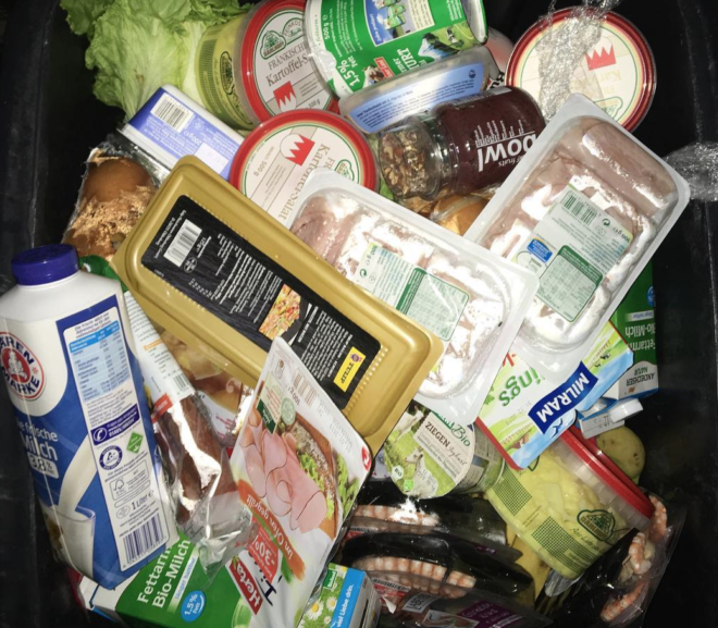 Eine Supermarkt Tonne gefüllt mit Essen von Joghurt zu Brotaufstrichen, Milch, vielen Packungen Wurst. Die Tonne ist bis oben hin mit Essen gefüllt. Fotografiert von Alex Cio