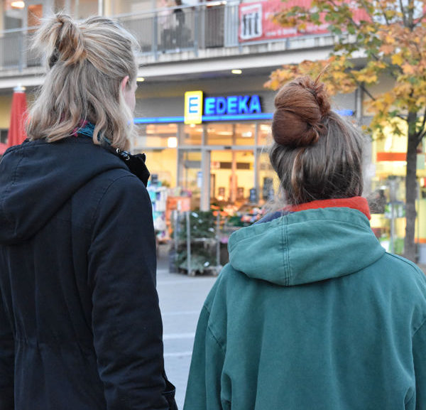Die beiden Studentinnen aus Olching die im Juni 2018 beim Containern erwischt wurden, hier von hinten zu sehen, wie sie vor einem Edeka Markt stehen, dessen Schild zwischen ihnen zu sehen ist.